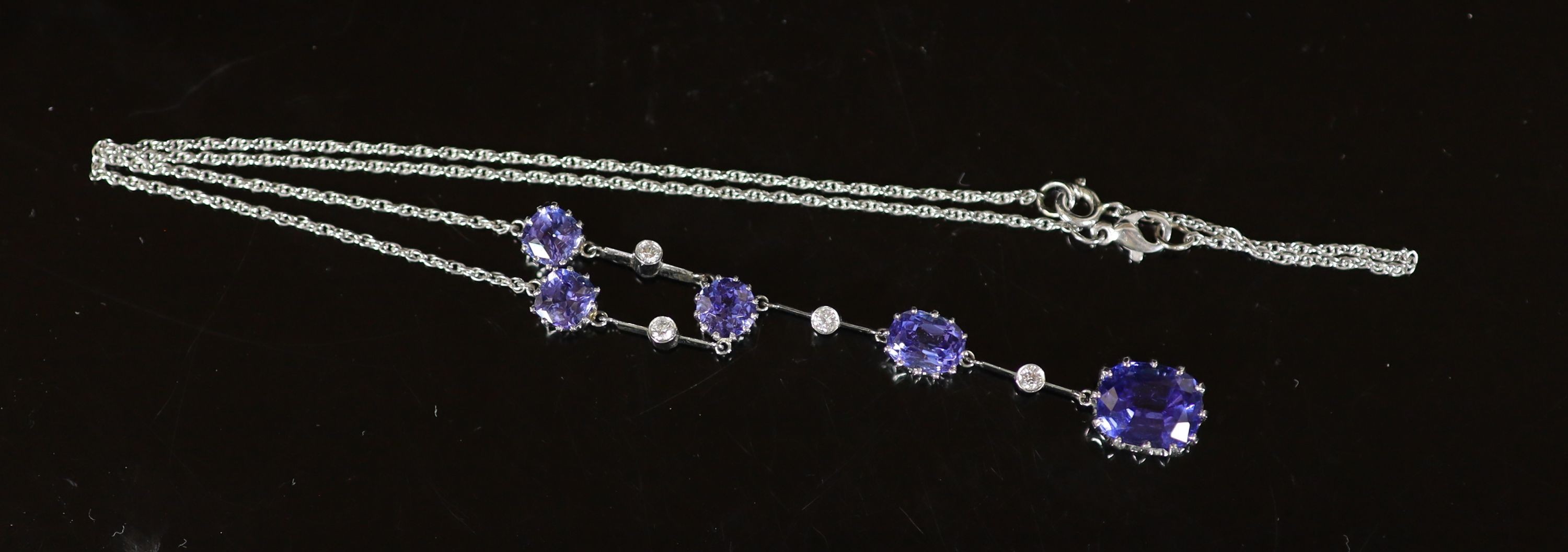 A modern platinum, five stone tanzanite and four small round cut diamond set drop pendant necklace